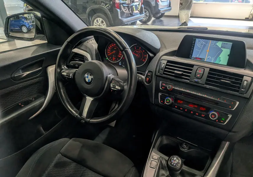 Vue intérieure côté conducteur de la BMW Série 1 F21 blanche, avec volant multifonction et écran de navigation visible.