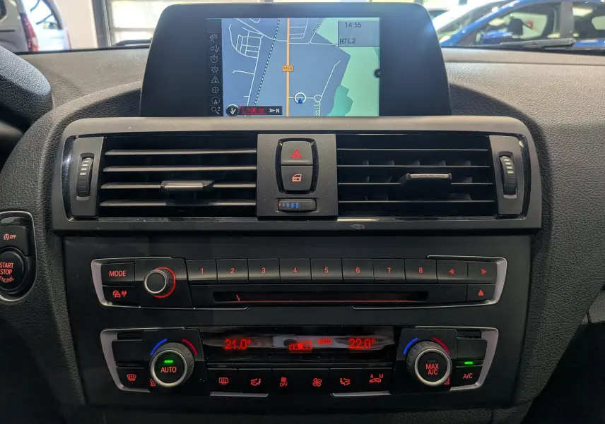 Tableau de bord intérieur de BMW Série 1 F21 blanc, vue frontale centrée sur la console avec écran GPS et commandes climatisation.