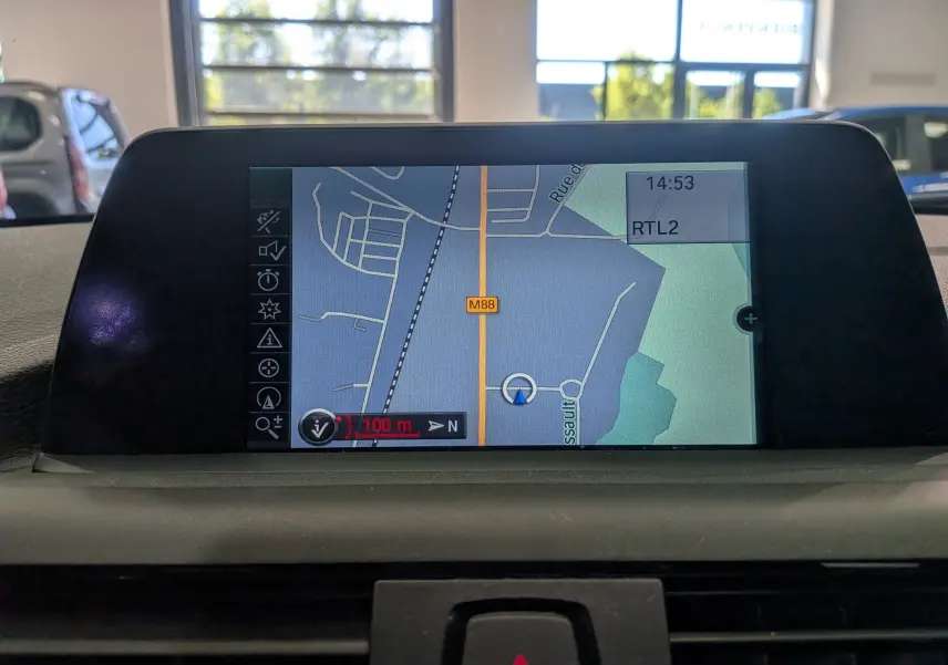 Écran central du GPS de la BMW Série 1 F21 blanc alpin, affichant une carte avec itinéraire en intérieur jour.