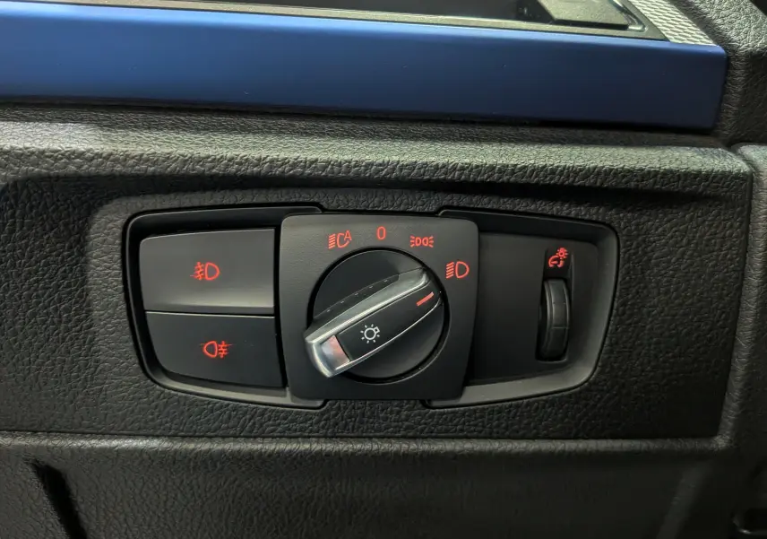 Gros plan sur le bouton de commande des phares avec éclairage rouge, intérieur noir de la BMW Série 1 F21 M Sport.