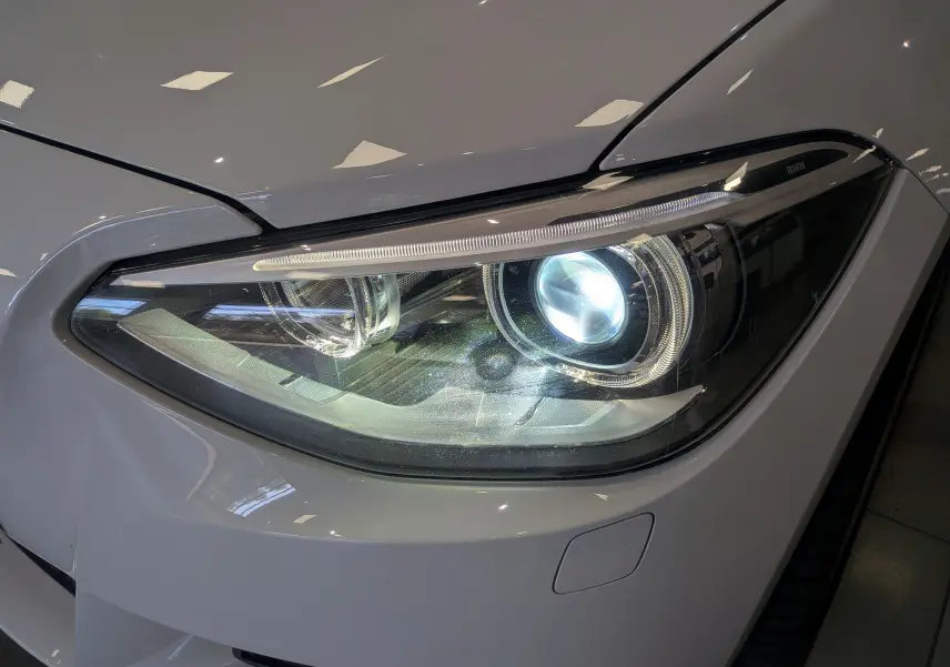 Gros plan sur le phare avant droit blanc alpin de la BMW Série 1 F21 118d xDrive M Sport 2014.