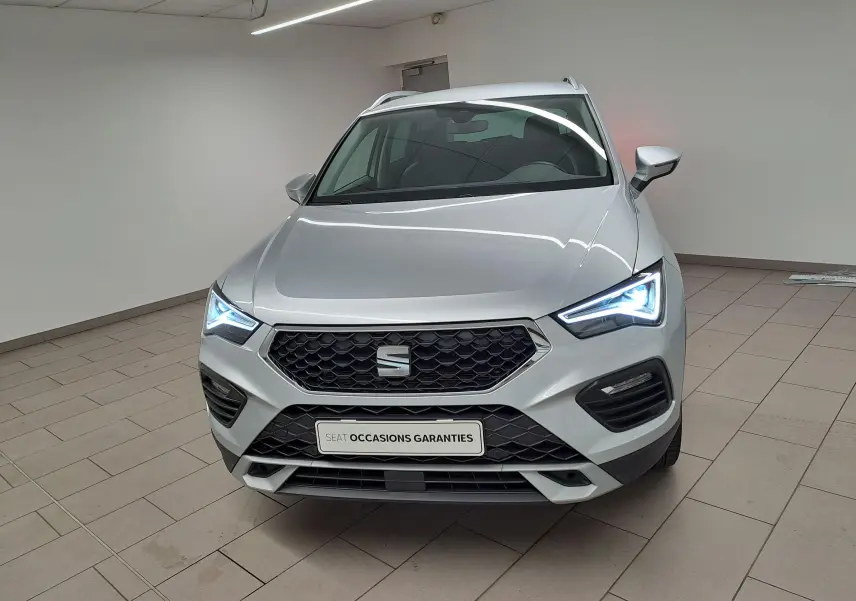 Vue avant d'un SEAT Ateca 2.0 TDI 150 DSG7 Copa argent Reflex avec feux LED allumés dans un showroom.