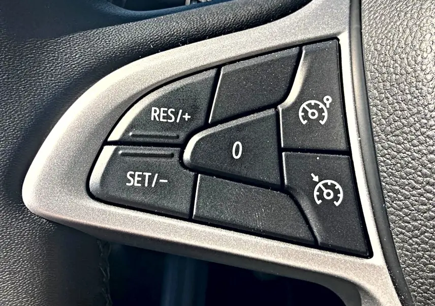 Gros plan sur les commandes noires du régulateur de vitesse sur le volant de la Dacia Sandero blanche.