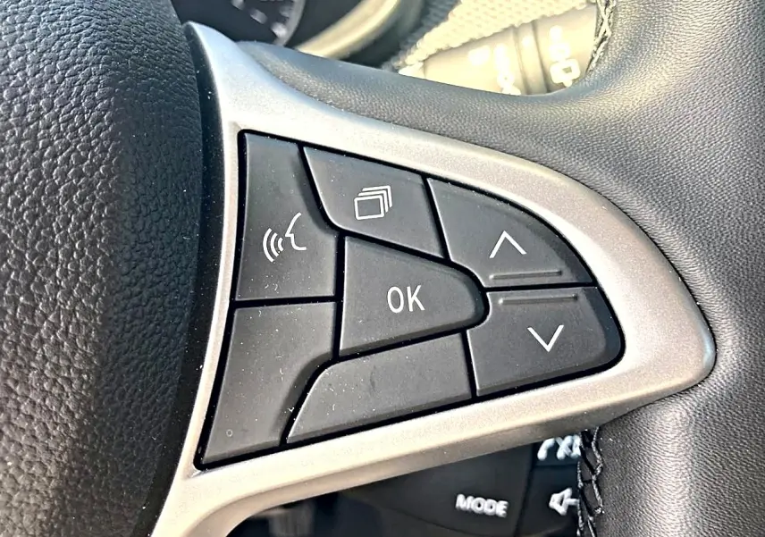 Gros plan sur les commandes noires du volant de la Dacia Sandero blanche, avec boutons multifonctions et finition argentée.