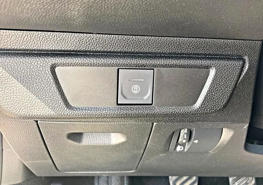 Gros plan sur le bouton de verrouillage centralisé noir dans l'habitacle de la Dacia Sandero blanche, côté conducteur.