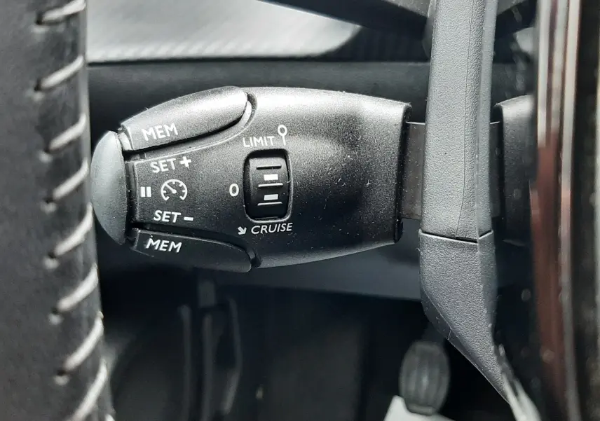 Gros plan sur la commande de régulateur de vitesse noire à gauche du volant dans une Peugeot 208 gris selenium 2024.