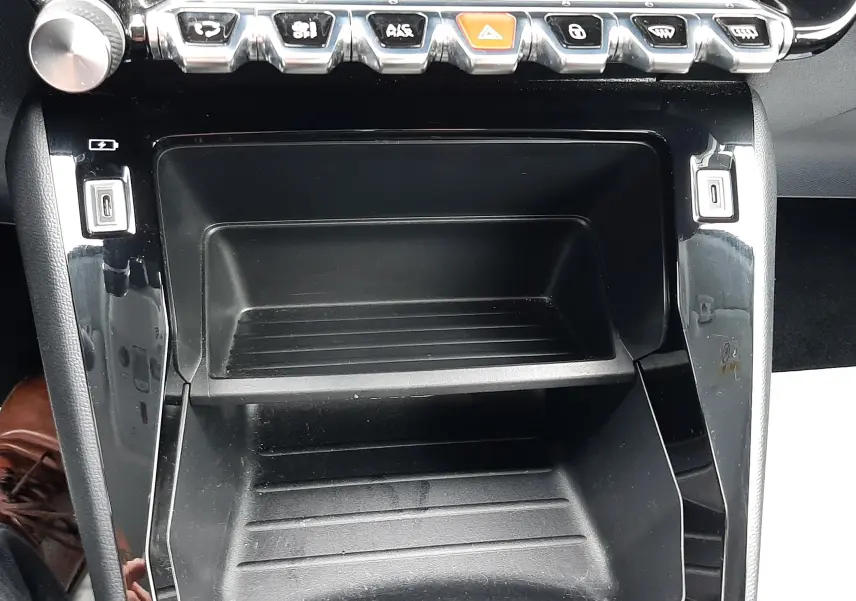 Vue rapprochée de la console centrale noire de la Peugeot 208 2024 avec rangements et rangée de boutons chromés.