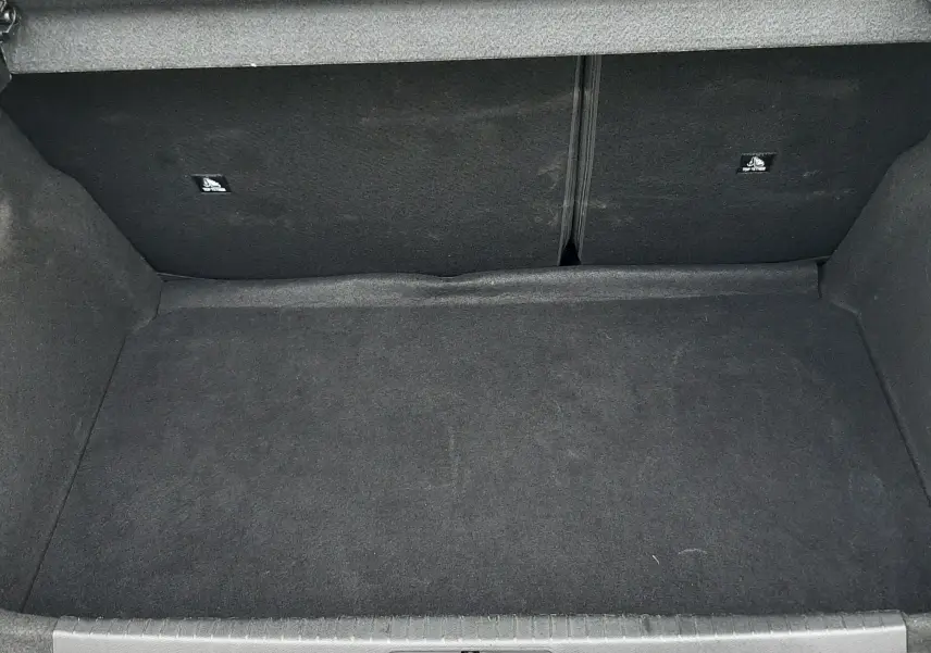 Coffre ouvert de la Peugeot 208 gris selenium 2024, vue plongeante sur l'espace de rangement vide et tapis noir.