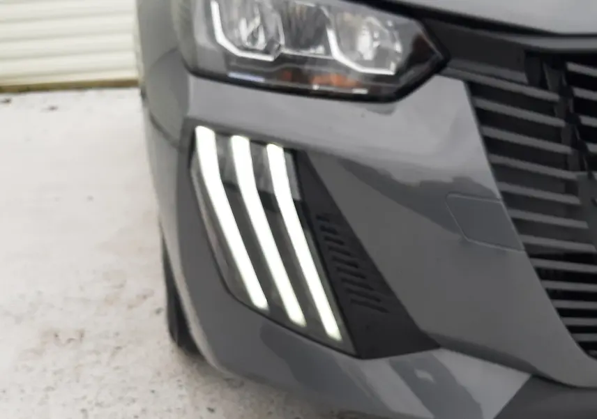 Gros plan sur l'avant droit gris sélénite du Peugeot 208 2024, mettant en valeur ses feux LED distinctifs en forme de griffes.