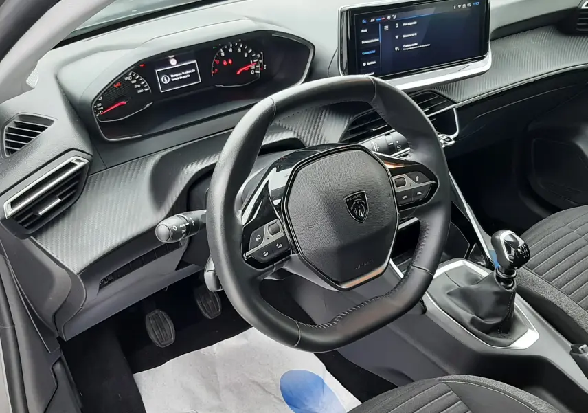 Vue intérieure côté conducteur de la Peugeot 208 2024 gris selenium, avec volant compact, tableau de bord numérique et écran tactile central.