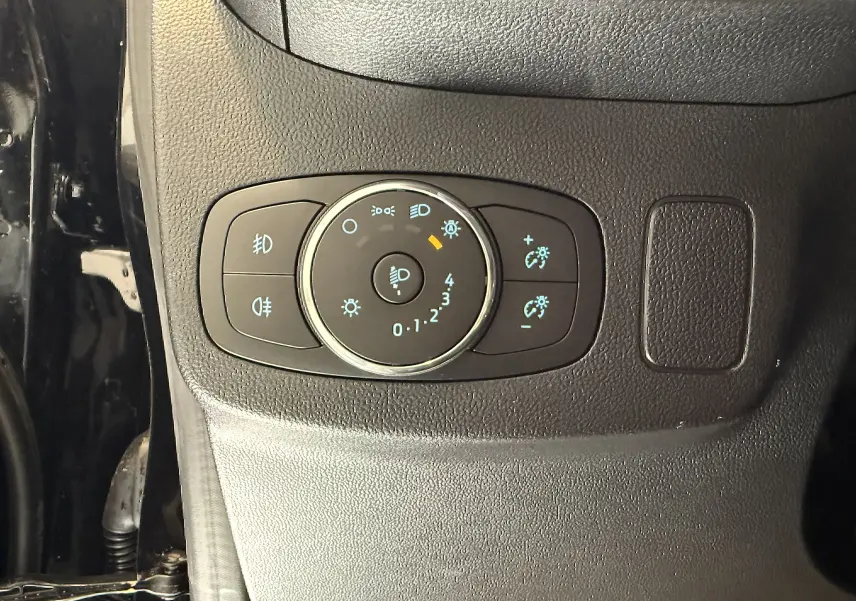 Gros plan sur le bouton de réglage des phares et des feux antibrouillard dans l’habitacle noir du Ford Puma noir agate.