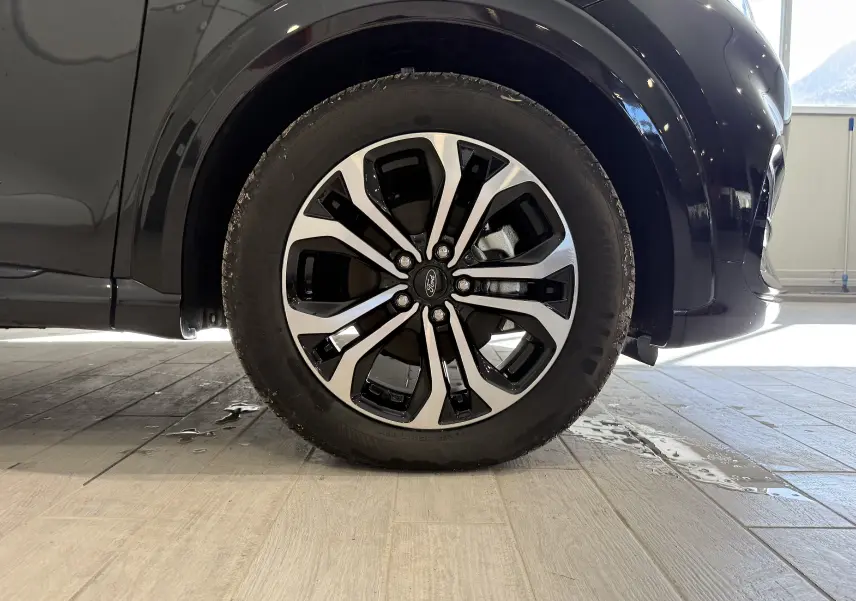 Gros plan sur la roue avant droite d’un Ford Puma noir Agate, mettant en valeur la jante alliage bicolore au design moderne.