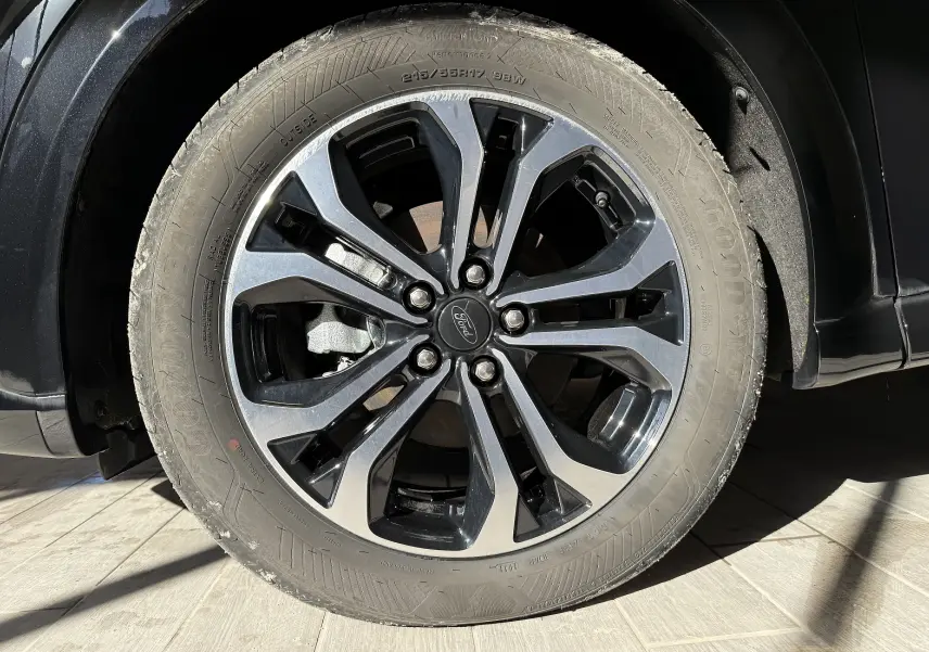 Gros plan sur la roue avant droite du Ford Puma noir Agate, mettant en valeur la jante alliage bicolore et le logo Ford central.