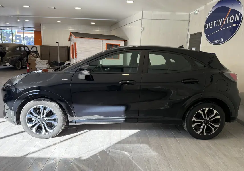 Vue de profil côté gauche d’un Ford Puma noir Agate 2022 avec jantes alliage et finition ST-Line en intérieur showroom.