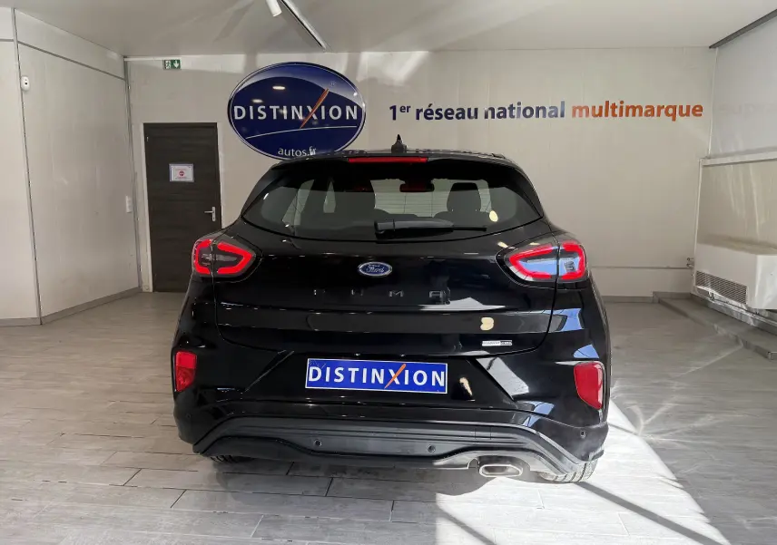 Vue arrière d'une Ford Puma noir agate 2022 avec feux LED distinctifs et sortie d'échappement visible en intérieur showroom.