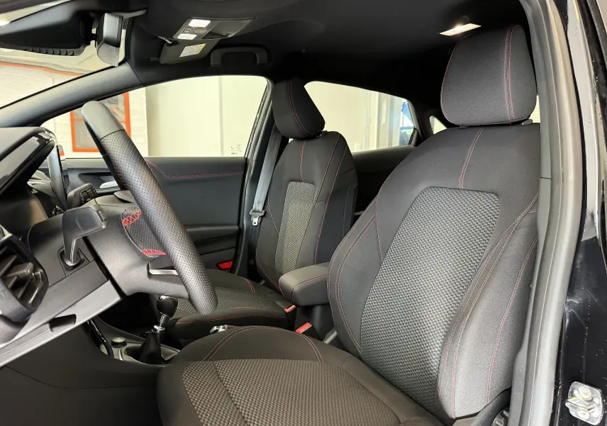 Vue intérieure côté gauche du Ford Puma noir Agate 2022, sièges tissu avec surpiqûres rouges et volant sport perforé.