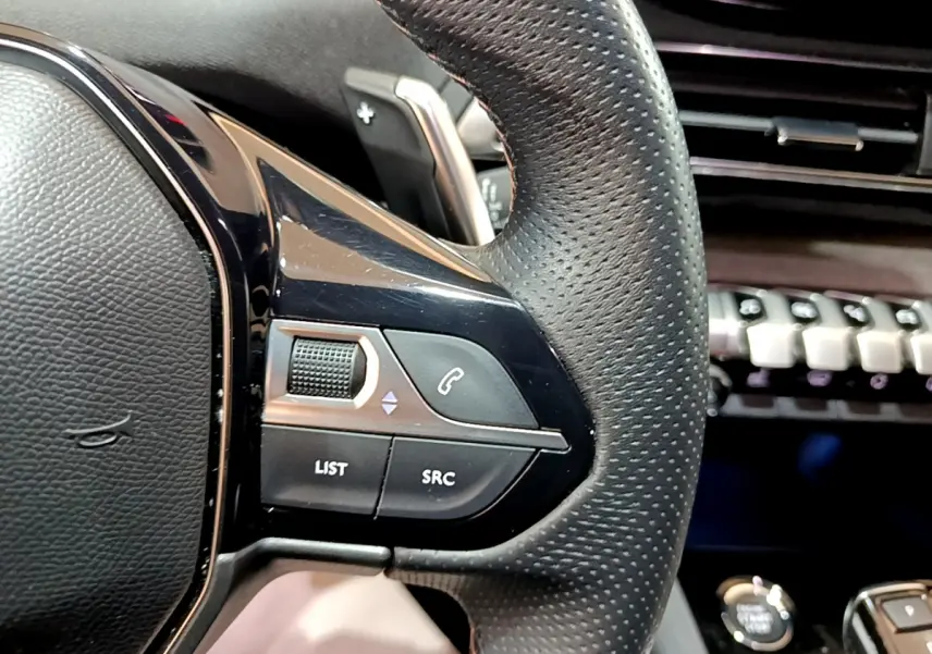 Gros plan sur le côté gauche du volant cuir noir du Peugeot 3008 2023 avec commandes audio et téléphone intégrées.