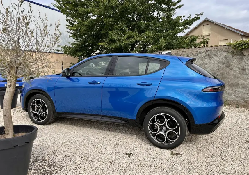 Vue de profil côté gauche d'un Alfa Romeo Tonale 1.5 mHEV Sprint bleu métallisé garé sur gravier, avec jantes distinctives.