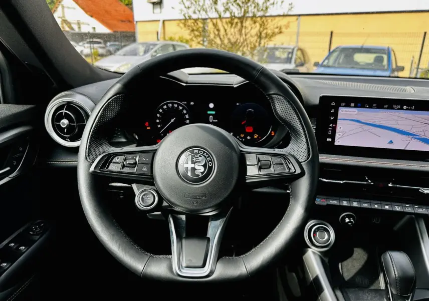 Vue intérieure centrée sur le volant cuir noir de l'Alfa Romeo Tonale 2024 avec tableau de bord digital et écran tactile GPS.