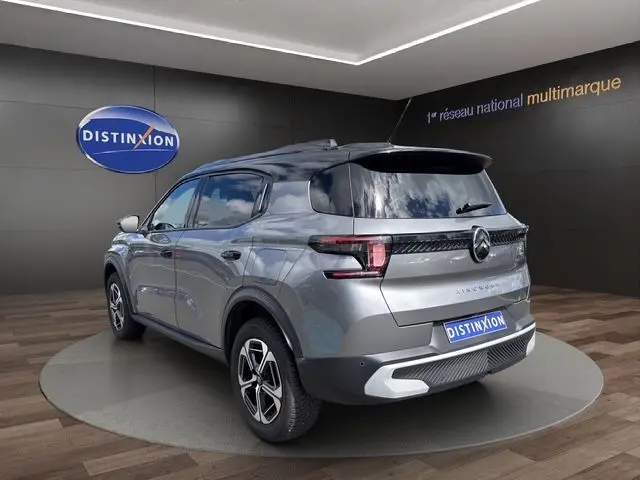 Vue 3/4 arrière droite d'un Citroën C3 Aircross gris mercury avec toit noir, barres de toit et feux arrière LED distinctifs.