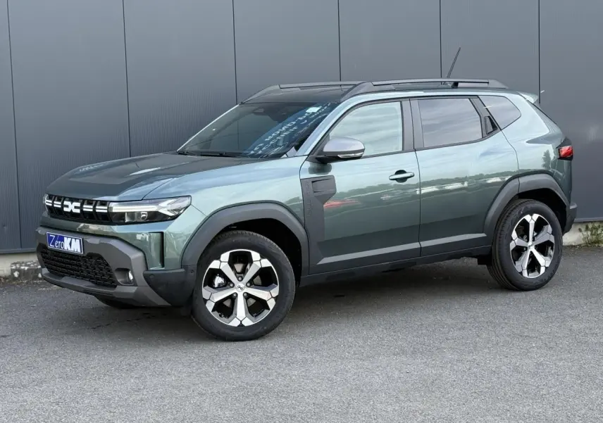 Vue 3/4 avant du Dacia Duster 2026 vert cèdre avec jantes alliage diamantées et barres de toit noires.