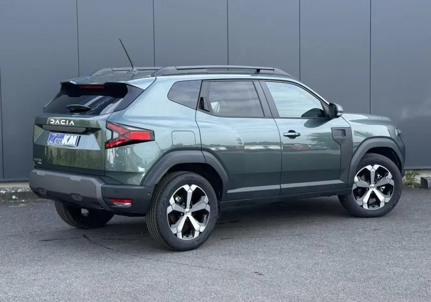 Vue 3/4 arrière droite du Dacia Duster 2026 vert cèdre avec jantes alliage diamantées et barres de toit noires.