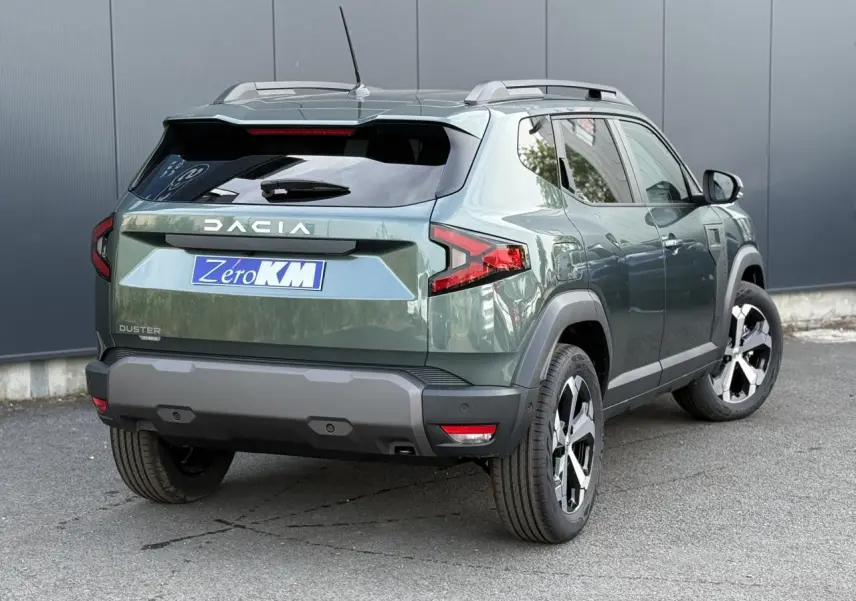 Vue 3/4 arrière droite du Dacia Duster 2026 vert cèdre avec jantes alliage diamantées et barres de toit argentées.