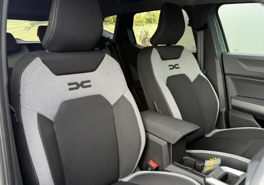 Vue intérieure des sièges avant gris et noirs du Dacia Duster 2026, avec accoudoir central et finitions contrastées.