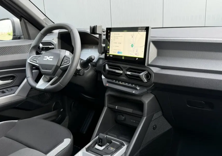 Vue intérieure côté conducteur du Dacia Duster 2026, avec tableau de bord noir et écran tactile central affichant la navigation.