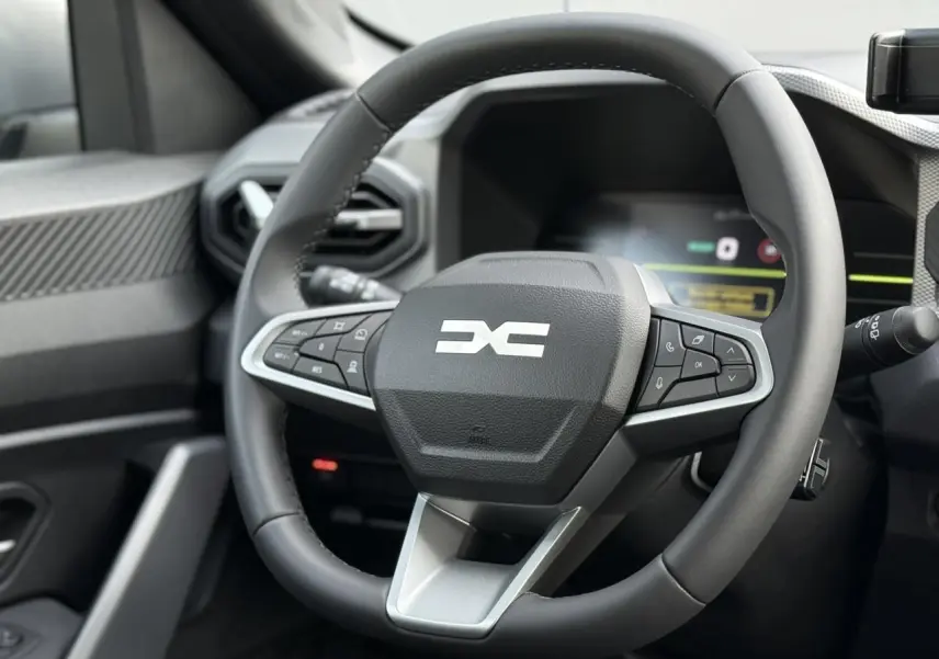 Vue rapprochée du volant noir du Dacia Duster 2026 avec commandes intégrées et tableau de bord digital en arrière-plan.