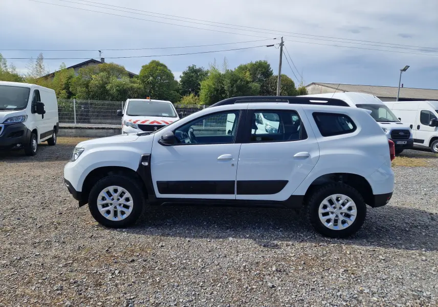 Profil droit du Dacia Duster 4x4 blanc 2022 avec protections noires et jantes alliage 16 pouces visible en extérieur.