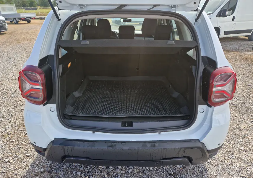 Vue arrière du coffre ouvert d'un Dacia Duster blanc 4x4 2022, montrant l'espace de chargement vide avec tapis en caoutchouc.
