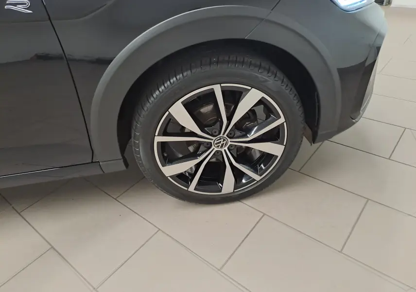 Gros plan sur la roue avant gauche du Volkswagen Taigo noir intense 2025 avec jante alliage léger 18'' Misano et logo R-Line visible.