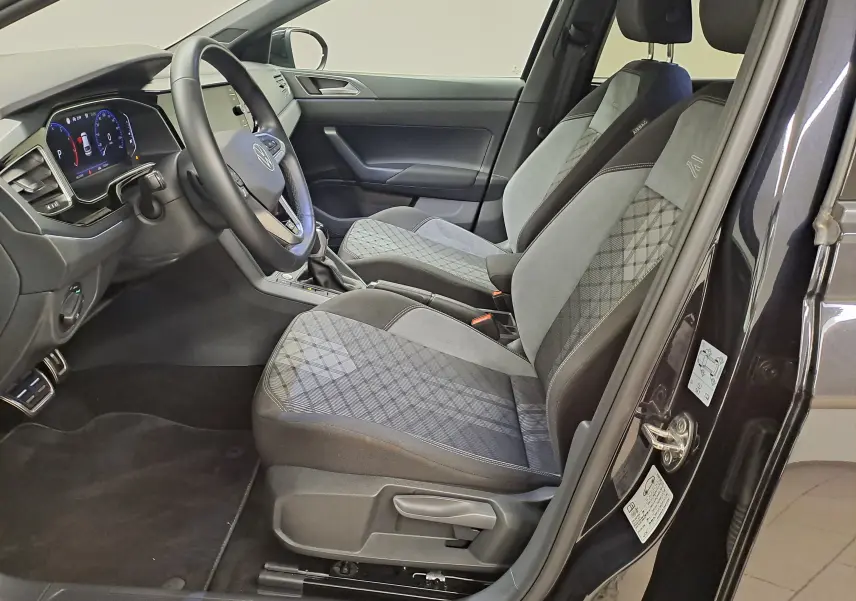 Vue intérieure côté conducteur du Volkswagen Taigo noir intense 2025, sièges tissu avec surpiqûres R-Line et tableau de bord digital.