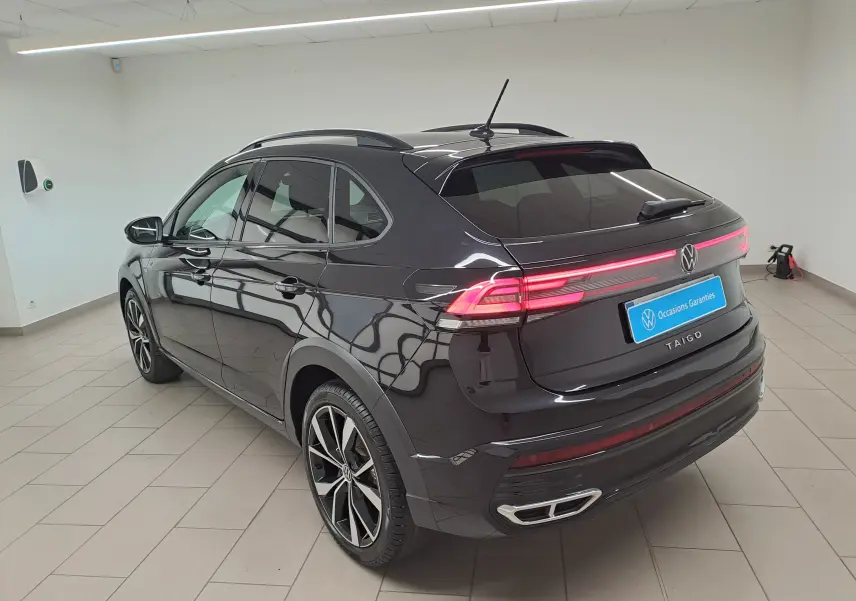 Vue 3/4 arrière droite d'un Volkswagen Taigo noir intense 2025 avec jantes alliage 18'' Misano et feux arrière allumés.