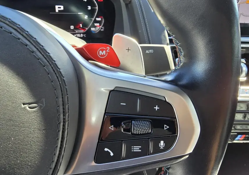 Gros plan sur le volant cuir noir avec palettes M rouges et commandes multifonctions d'une BMW Série 8 Cabriolet M8 Competition.