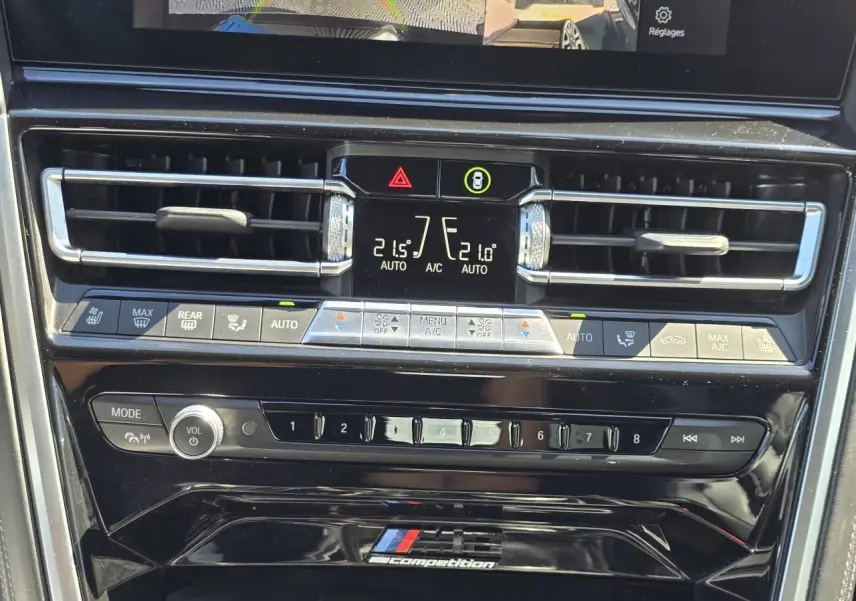 Détail de la console centrale noire brillante avec commandes climatisation et logo M8 Competition d'une BMW Série 8 Cabriolet noire.