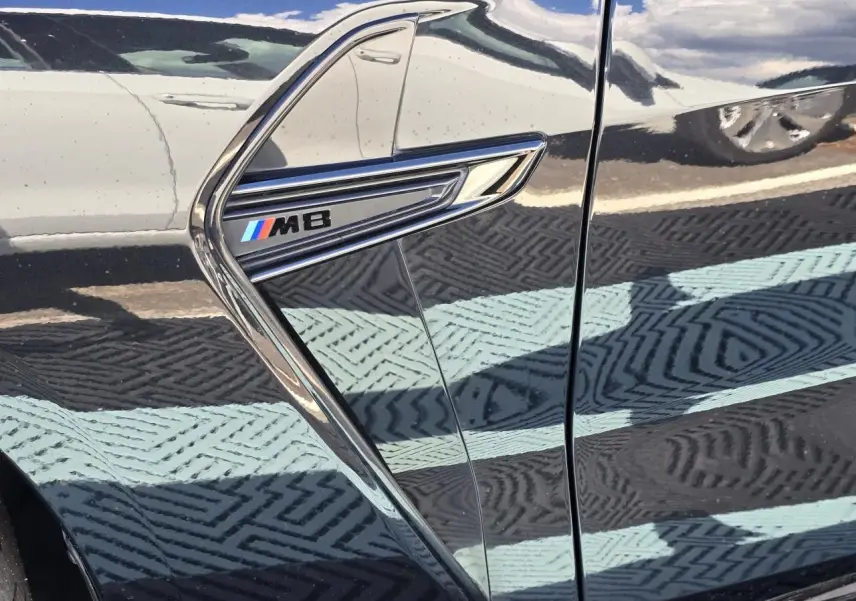 Détail de l'aile avant gauche noire saphir métal d'une BMW M8 avec logo M8 chromé et bleu rouge blanc.