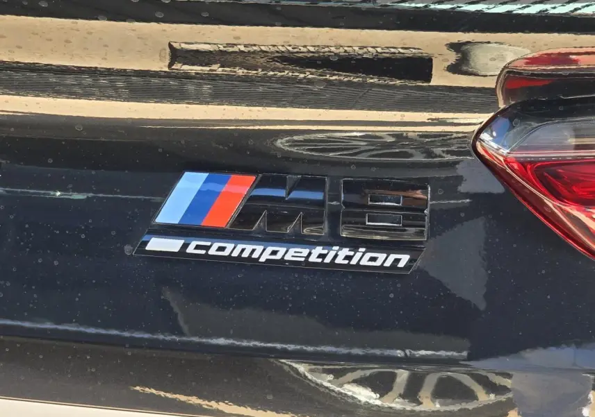 Gros plan sur l'emblème M8 Competition noir brillant sur la malle arrière d'une BMW Série 8 Cabriolet noir saphir métal.