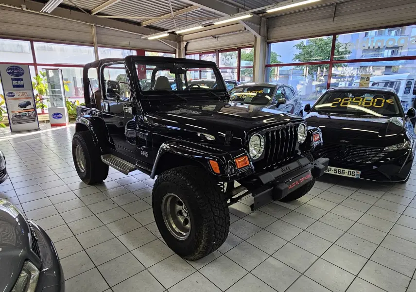 Jeep Wrangler noir vue 3/4 avant droit en intérieur, avec toit ouvert et pneus tout-terrain visibles.