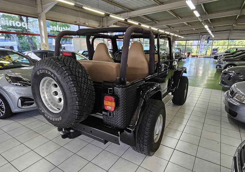 Vue 3/4 arrière droite du Jeep Wrangler noir 2000 avec intérieur beige et roue de secours montée à l'arrière.