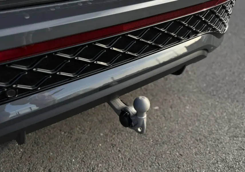 Gros plan sur l'attelage rabattable gris dauphin du Volkswagen Tayron 2025, avec calandre noire R-Line visible.