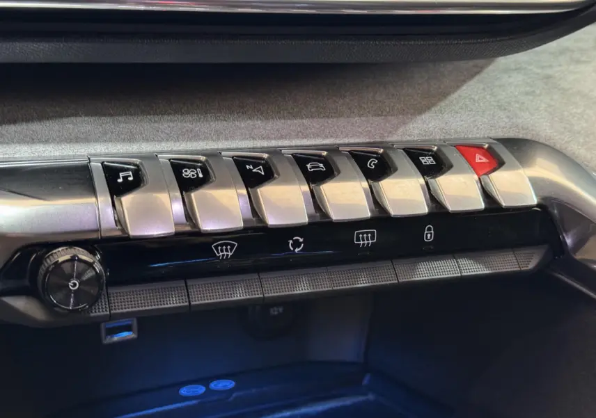 Gros plan sur la rangée de boutons argentés et noirs du tableau de bord du Peugeot 3008 gris clair, version GT.