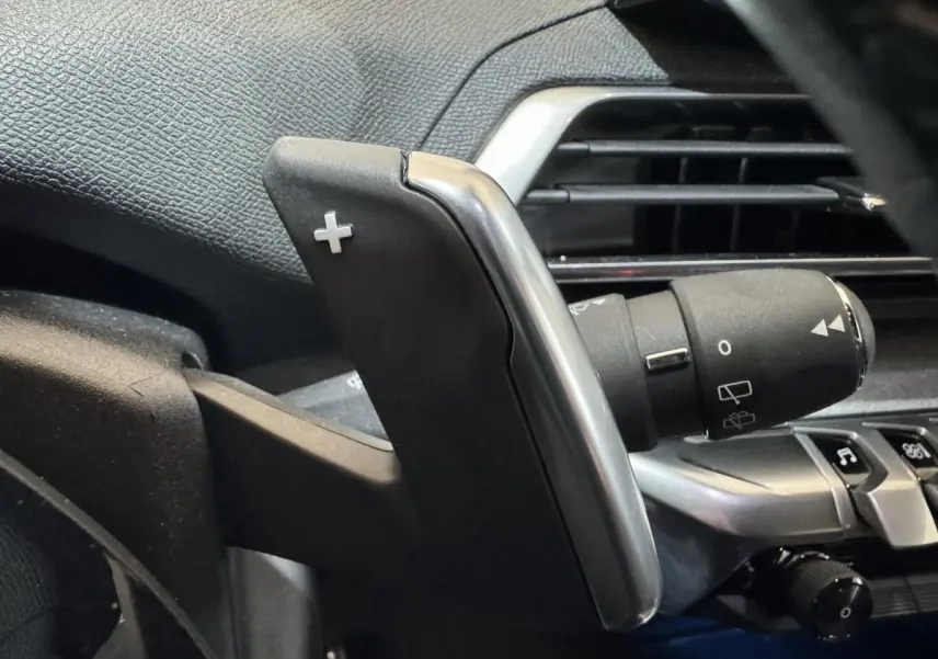Gros plan sur la palette de changement de vitesse droite en plastique noir et métal dans l'habitacle du Peugeot 3008 gris clair.