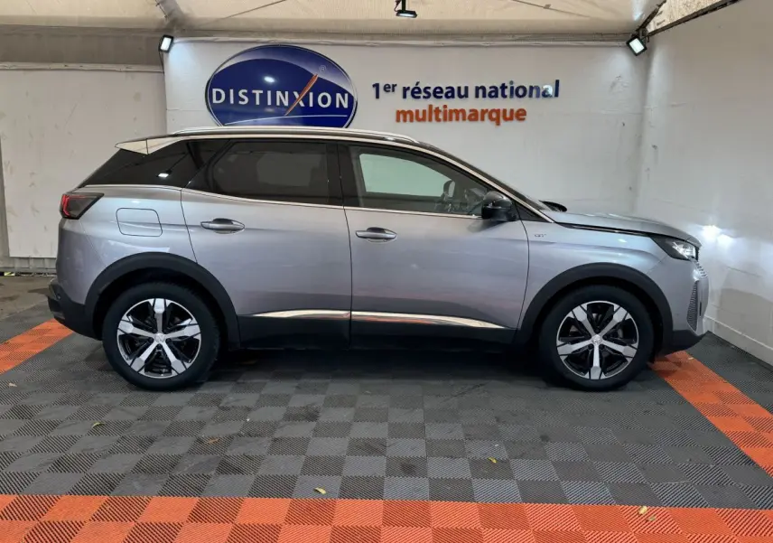 Profil droit d'un Peugeot 3008 gris clair version GT, avec jantes alliage et toit noir dans un garage.