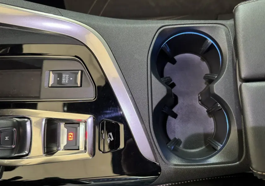 Gros plan sur la console centrale noire brillante du Peugeot 3008 gris clair, avec commandes de frein à main et porte-gobelets.