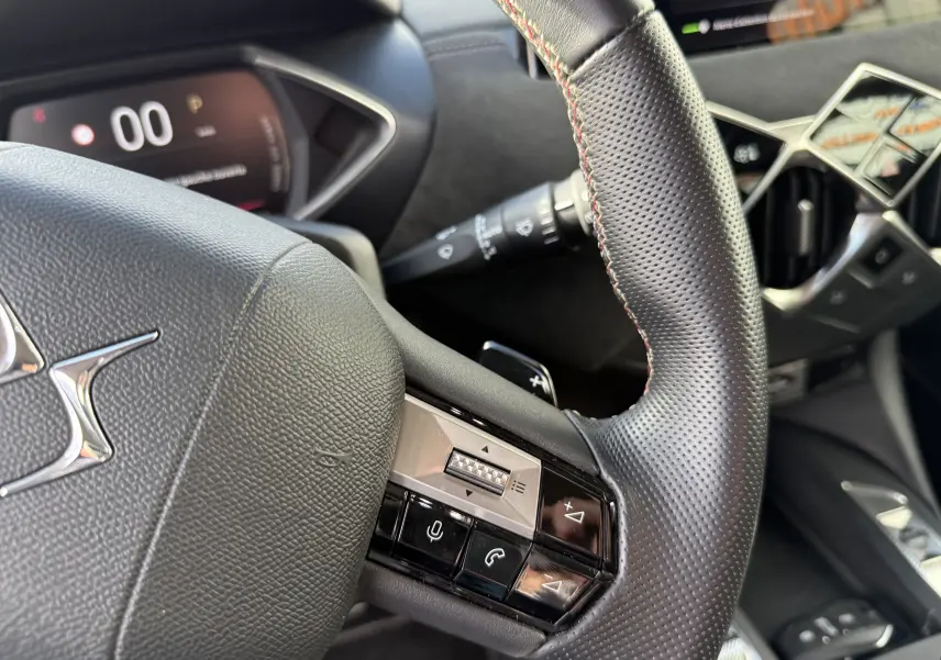 Gros plan sur le volant en cuir noir perforé du DS3 hybride 2025 avec commandes intégrées et tableau de bord numérique.