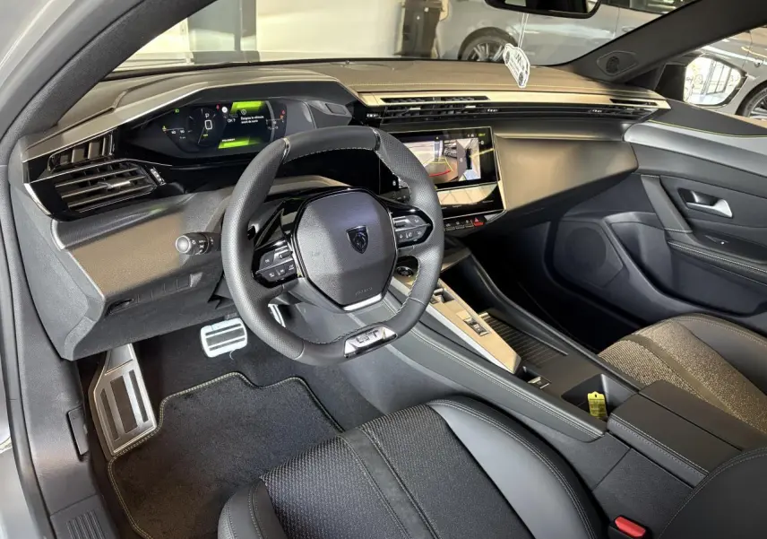 Intérieur avant droit de la Peugeot 308 GT 2025 avec volant cuir, combiné numérique et sellerie tri matières noire.