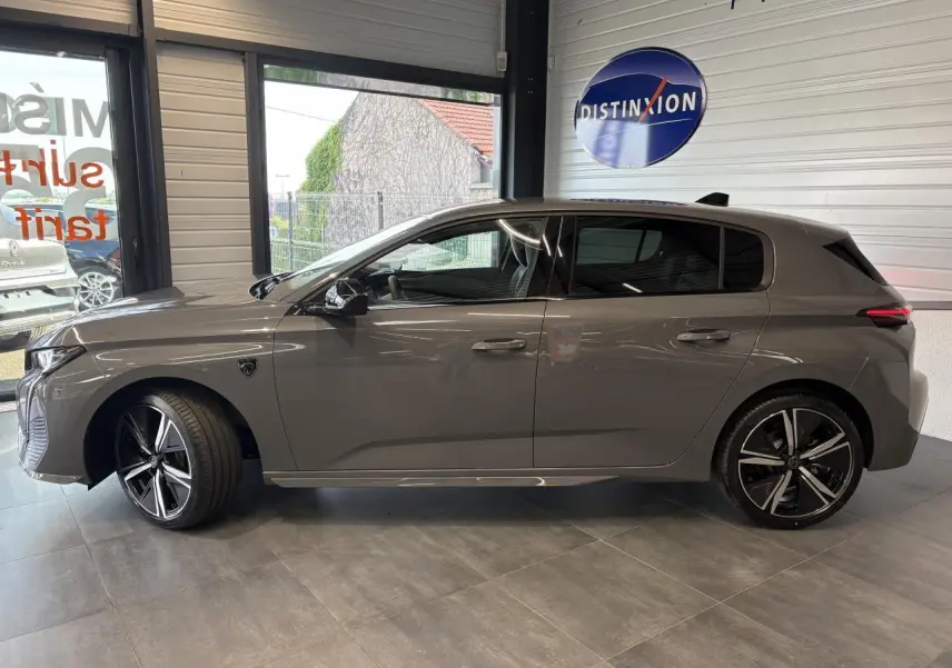 Profil droit de la Peugeot 308 GT 2025 gris selenium avec jantes alliage 18'' et vitres surteintées en showroom.