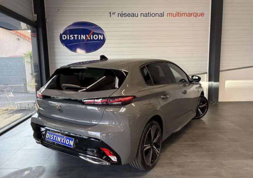 Vue 3/4 arrière droite d'une Peugeot 308 GT 2025 gris selenium avec jantes alliage 18'' et bandeau noir brillant arrière.